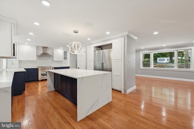 kitchen featuring a kitchen island, decorative light fixtures, high quality appliances, wall chimney range hood, and white cabinets