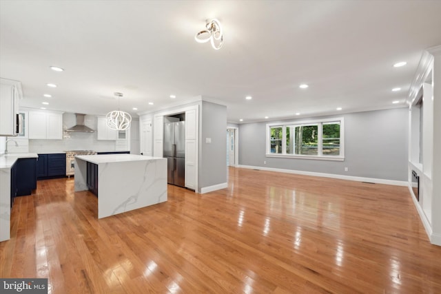 kitchen featuring blue cabinetry, a kitchen island, hanging light fixtures, white cabinets, and wall chimney range hood