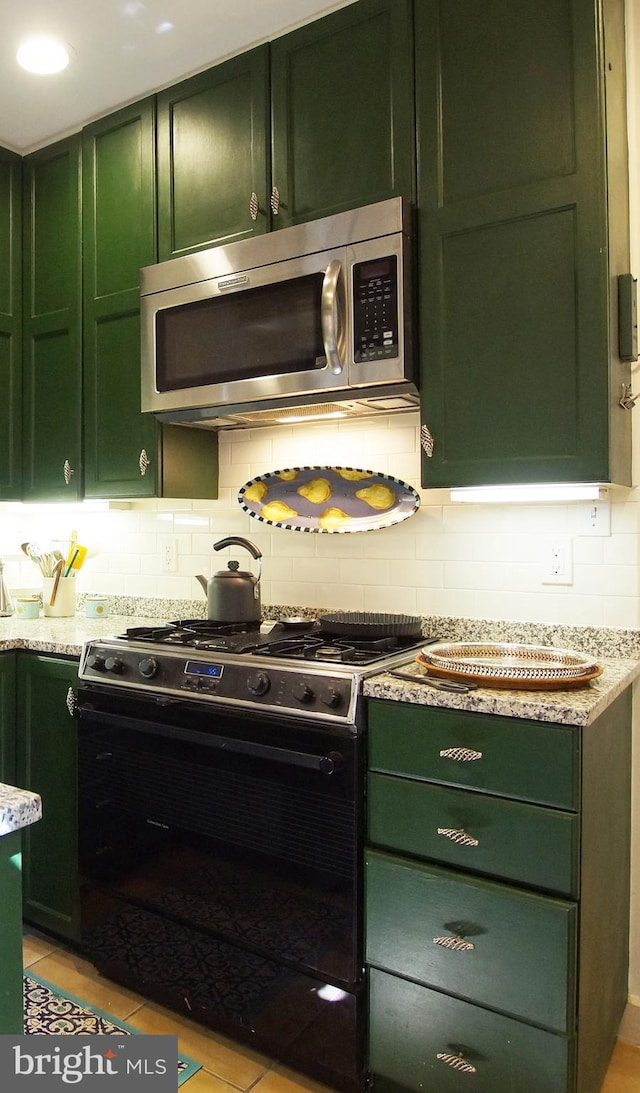 kitchen with light stone counters, black gas range oven, green cabinets, backsplash, and light tile patterned floors