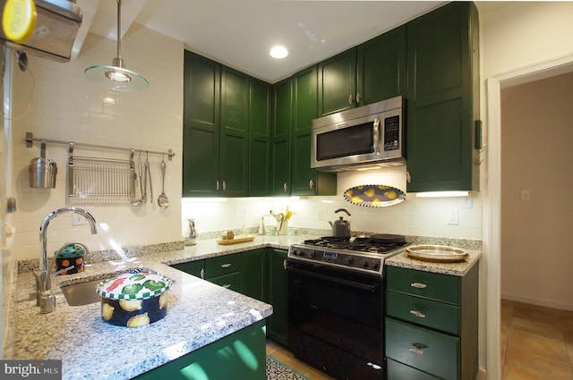 kitchen featuring green cabinetry, backsplash, decorative light fixtures, black gas range, and light stone countertops