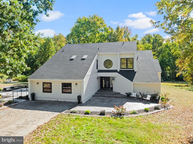 modern farmhouse with a front lawn, fence, concrete driveway, roof with shingles, and a patio