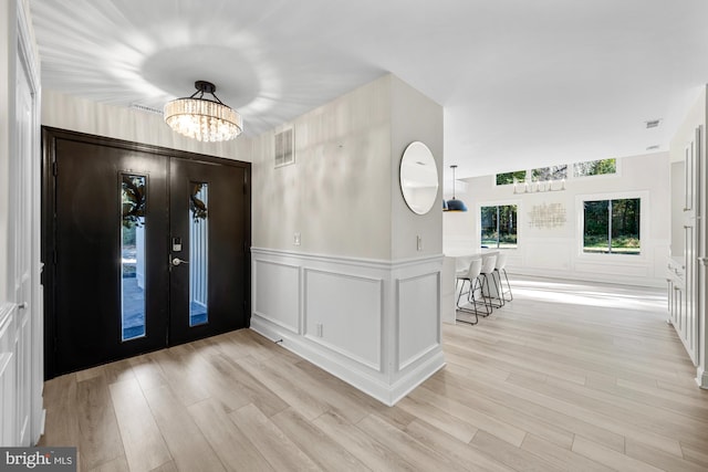 foyer featuring visible vents, a decorative wall, a wainscoted wall, light wood-style flooring, and a notable chandelier