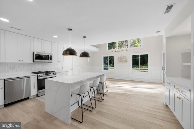 kitchen with visible vents, backsplash, a kitchen bar, white cabinets, and stainless steel appliances