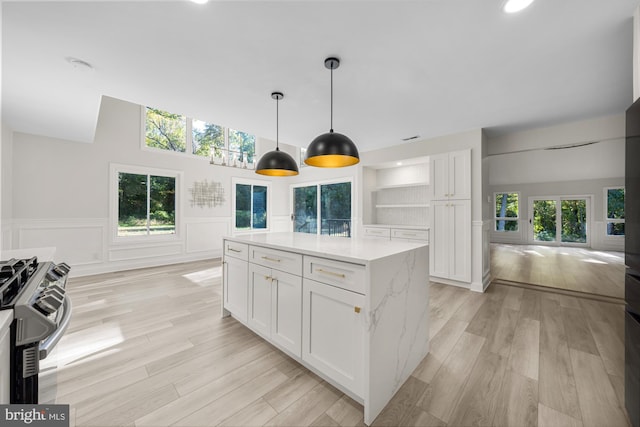 kitchen featuring open shelves, stainless steel gas range, white cabinetry, light wood finished floors, and pendant lighting