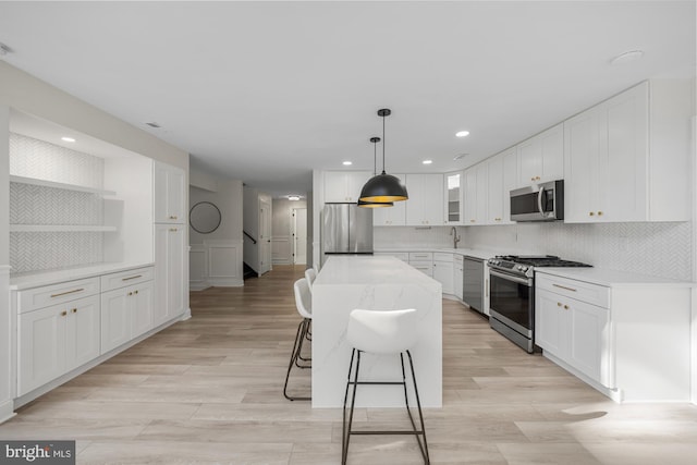 kitchen with white cabinets, open shelves, stainless steel appliances, a kitchen island, and a breakfast bar area