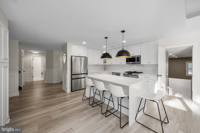 kitchen featuring stainless steel appliances, a breakfast bar area, white cabinets, and light countertops