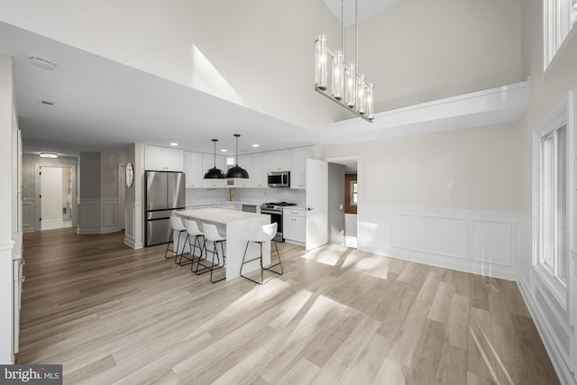 kitchen with a high ceiling, light countertops, white cabinetry, a breakfast bar area, and stainless steel appliances