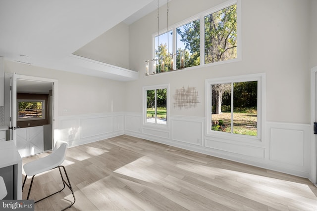 unfurnished dining area featuring light wood finished floors, wainscoting, a towering ceiling, and a healthy amount of sunlight