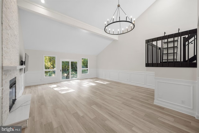 unfurnished living room featuring a large fireplace, beamed ceiling, a notable chandelier, and wood finished floors