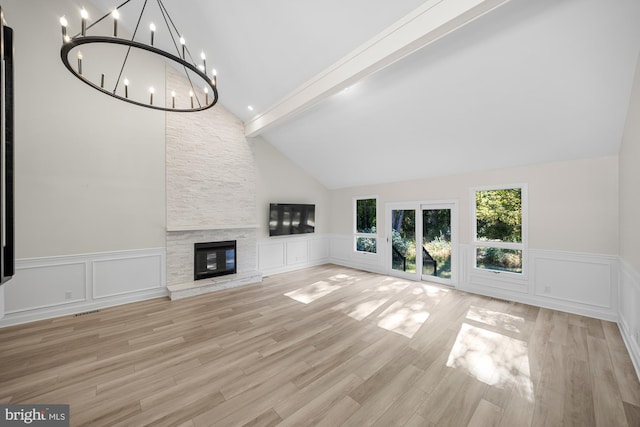 unfurnished living room with light wood-type flooring, a stone fireplace, a chandelier, and a decorative wall