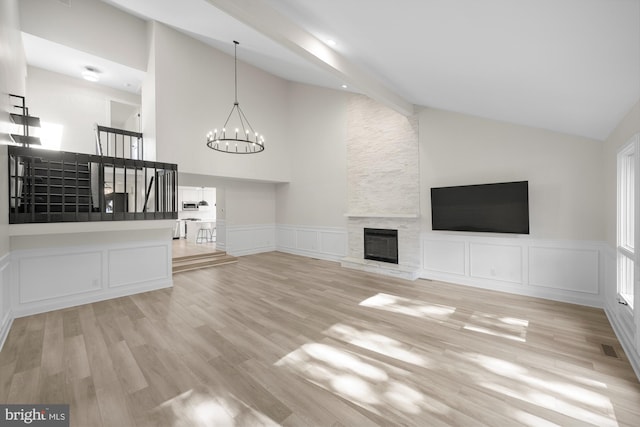 unfurnished living room featuring wood finished floors, visible vents, a stone fireplace, a decorative wall, and a notable chandelier