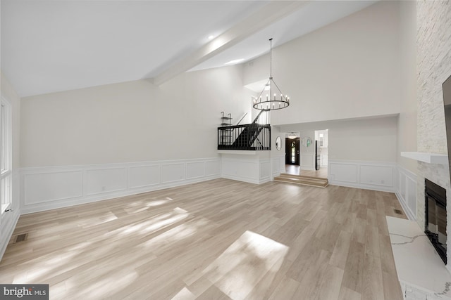 unfurnished living room with a stone fireplace, light wood-style flooring, visible vents, beamed ceiling, and a decorative wall