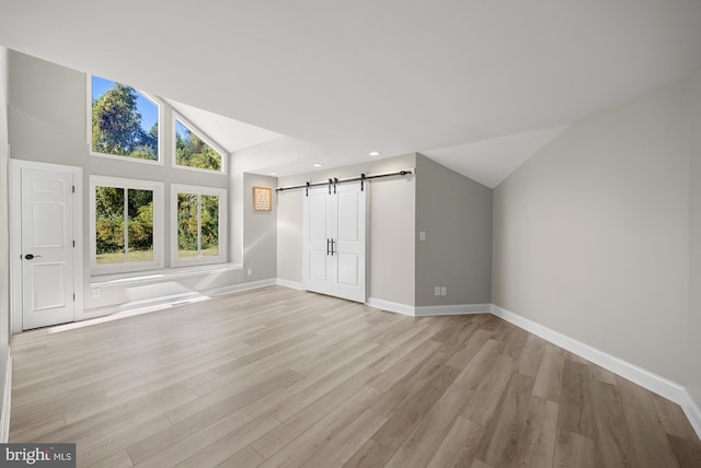 interior space featuring baseboards, light wood finished floors, recessed lighting, vaulted ceiling, and a barn door