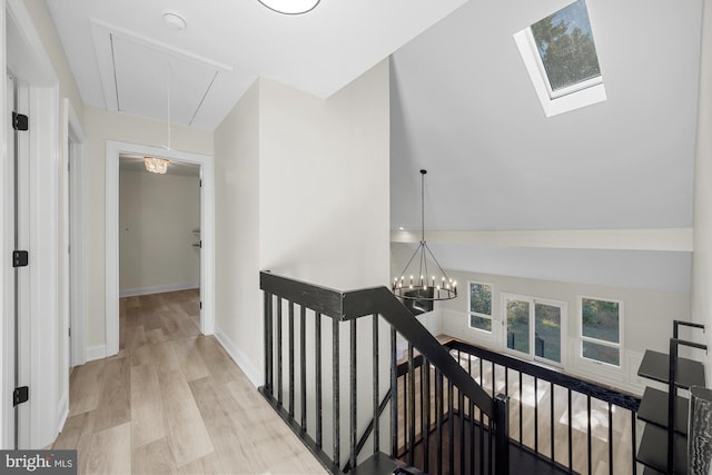 hall with wood finished floors, baseboards, attic access, a notable chandelier, and an upstairs landing