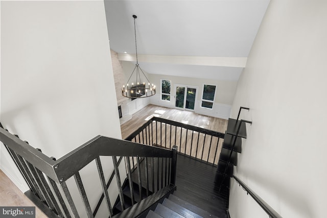 stairway with a chandelier, wood finished floors, and lofted ceiling