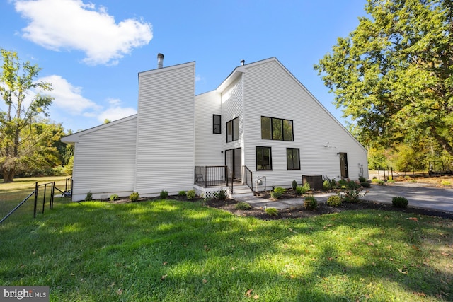 rear view of house featuring a chimney, fence, and a lawn