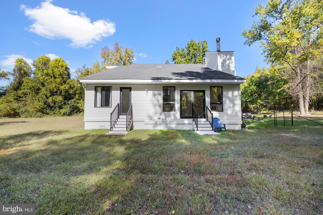 rear view of property with entry steps, roof with shingles, a yard, and a chimney