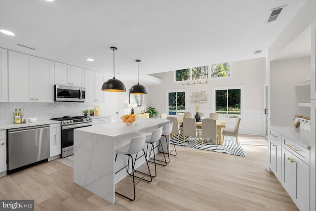 kitchen with a breakfast bar area, visible vents, decorative backsplash, appliances with stainless steel finishes, and white cabinetry