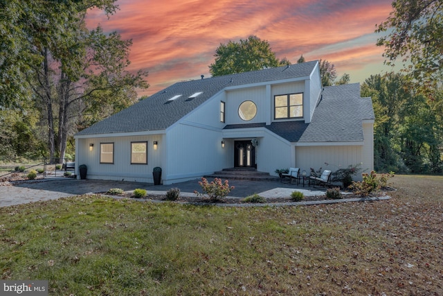 view of front of property with a patio area, a yard, and roof with shingles