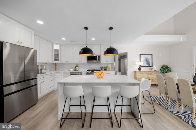 kitchen with tasteful backsplash, light wood-style floors, appliances with stainless steel finishes, and a breakfast bar area