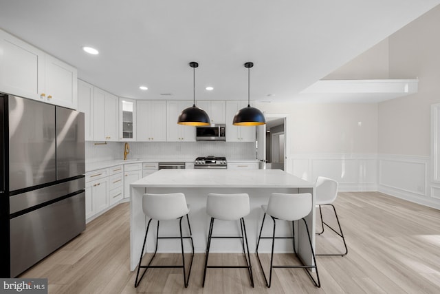 kitchen featuring a wainscoted wall, a kitchen island, white cabinets, a breakfast bar area, and stainless steel appliances
