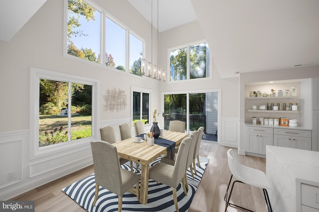 dining room with a notable chandelier, light wood-style flooring, a wainscoted wall, high vaulted ceiling, and a decorative wall