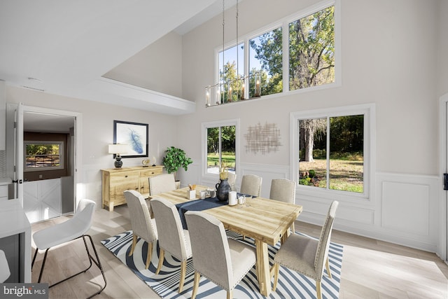 dining room featuring a notable chandelier, light wood-type flooring, a towering ceiling, and wainscoting