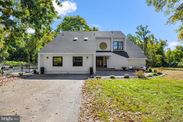 view of front of home with driveway, fence, roof with shingles, a front yard, and a patio area