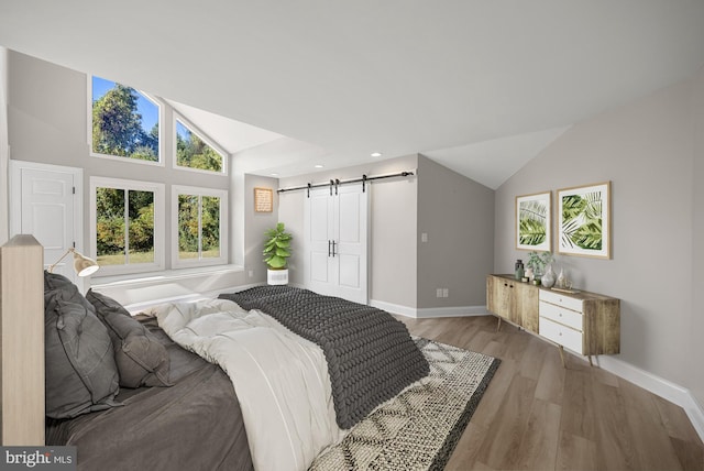 bedroom with a barn door, light wood-style flooring, baseboards, and vaulted ceiling