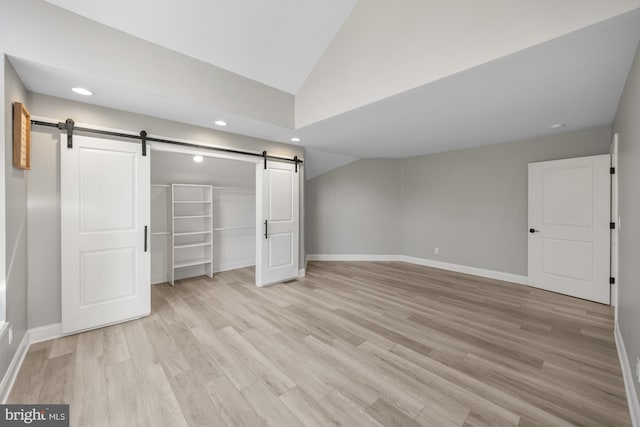 unfurnished bedroom featuring baseboards, light wood-type flooring, a barn door, and vaulted ceiling