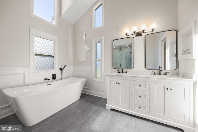 bathroom featuring a sink, a freestanding bath, double vanity, and wainscoting