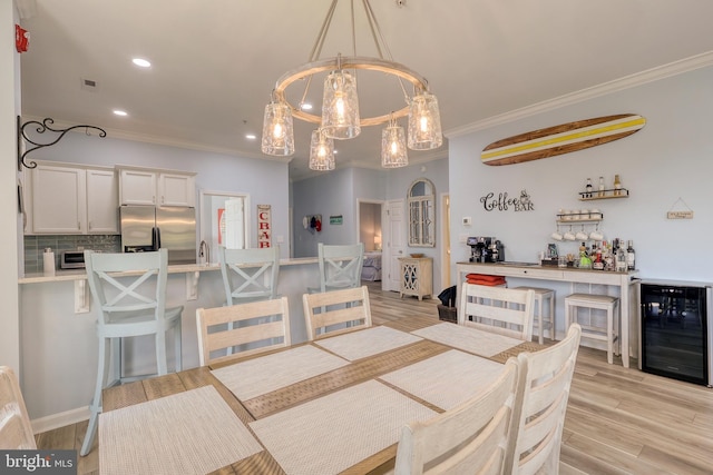 dining area featuring crown molding, wine cooler, a notable chandelier, and light hardwood / wood-style floors