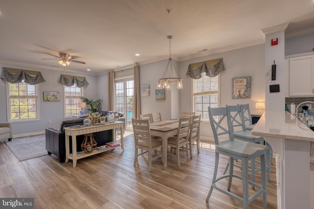 dining area featuring light wood-type flooring, ceiling fan with notable chandelier, ornamental molding, and a healthy amount of sunlight