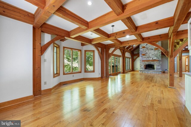 unfurnished living room featuring coffered ceiling, light hardwood / wood-style floors, beamed ceiling, and a stone fireplace