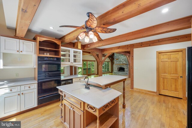 kitchen featuring black double oven, an island with sink, ceiling fan, light wood-type flooring, and white cabinets