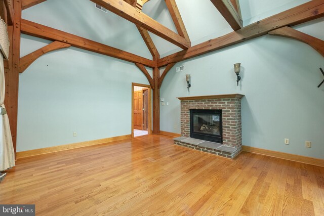 unfurnished living room featuring light wood-type flooring, high vaulted ceiling, and a brick fireplace