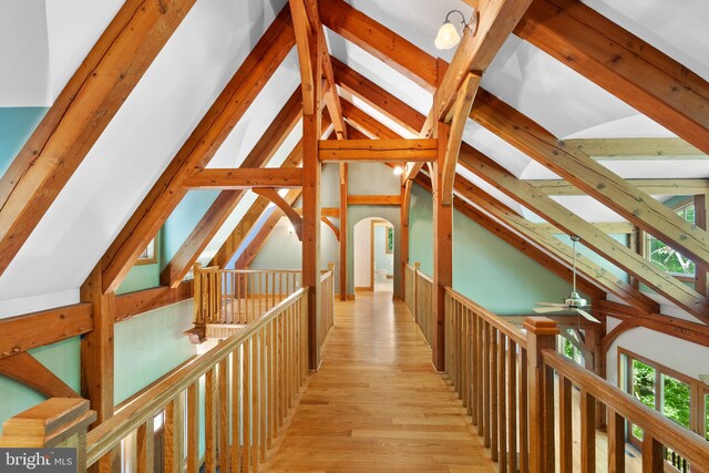 corridor with light wood-type flooring and lofted ceiling with beams