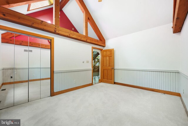 empty room featuring carpet, beamed ceiling, high vaulted ceiling, and a skylight