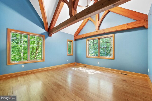 empty room with hardwood / wood-style flooring, a healthy amount of sunlight, and vaulted ceiling with beams