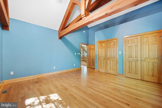 unfurnished bedroom with high vaulted ceiling, wood-type flooring, and multiple closets