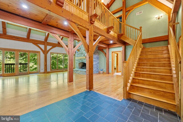 interior space featuring dark wood-type flooring, beamed ceiling, a stone fireplace, and high vaulted ceiling