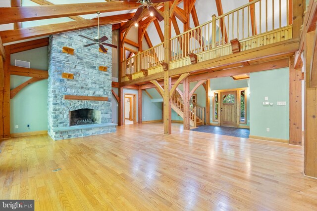 unfurnished living room featuring hardwood / wood-style floors, a stone fireplace, beam ceiling, high vaulted ceiling, and ceiling fan