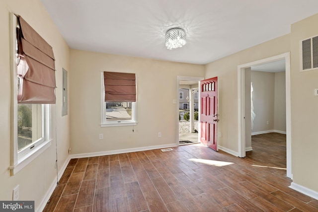 unfurnished room featuring an inviting chandelier, electric panel, plenty of natural light, and dark hardwood / wood-style flooring