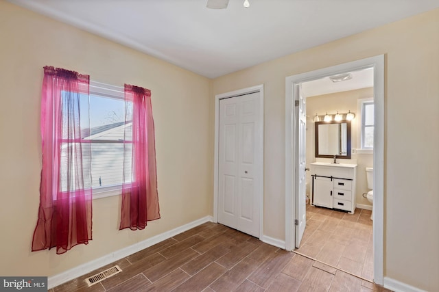 unfurnished bedroom featuring a closet, connected bathroom, multiple windows, and sink