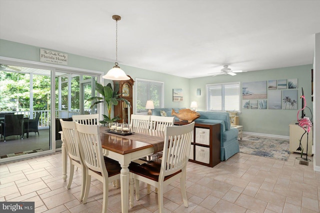 dining room featuring a wealth of natural light, baseboards, a ceiling fan, and stone finish floor