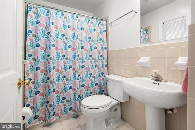 bathroom with curtained shower, toilet, wainscoting, tile patterned floors, and tile walls