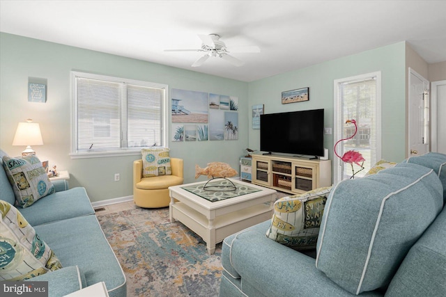 living area with baseboards and ceiling fan