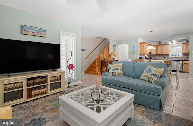 living room featuring ceiling fan, stairway, and stone tile flooring