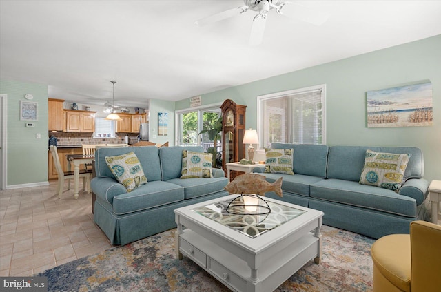 living room featuring baseboards, a ceiling fan, and stone finish floor