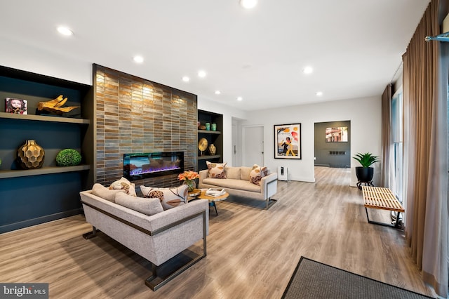 living area with light wood-style flooring, built in shelves, a large fireplace, and recessed lighting